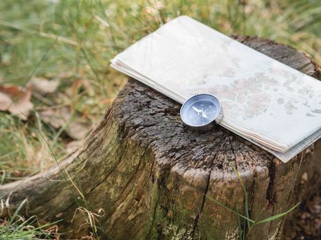 Compass and map lie on stump in forest. Tourist's gear for hiking. Summer adventure. Outdoor recreation. Active lifestyle.