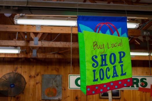 A Hanging Sign in a Wooden Farmer's Market That Says Buy Local Shop Local