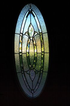 Stained glass window with iron detail and a blue sky with green grass beyond it in tropical architecture.