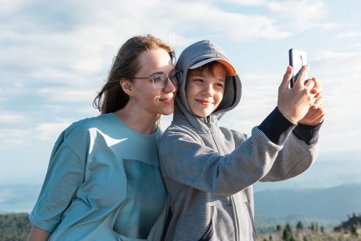 A child takes a selfie on a smartphone with mom in the mountain trip.