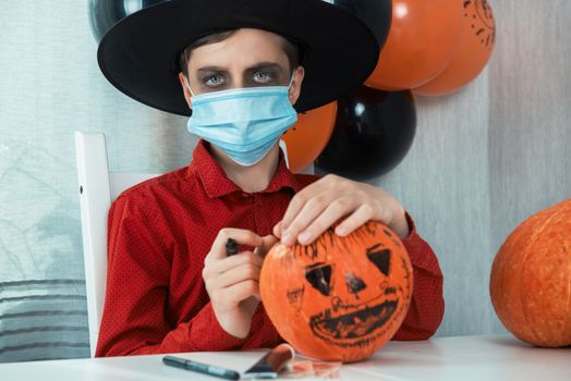 Teen boy in costume and face masks to protect against COVID-19 drawing a pumpkin for the Halloween celebration. Halloween carnival with new reality with pandemic concept.