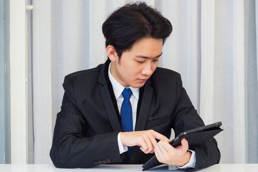 Work from home, Asian young businessman video conference call or facetime he smiling looking to camera sitting on desk using smart digital tablet computer touching on screen at home office