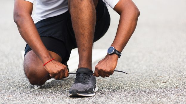 Close up Asian sport runner black man wear watch sitting he trying shoelace running shoes getting ready for jogging and run outdoor street health park with copy space, healthy exercise workout concept