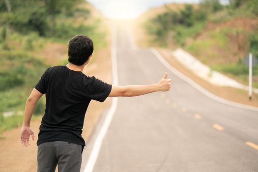 Man hitchhiking on the road, empty rural curve, asphalt road way. Rear view.
