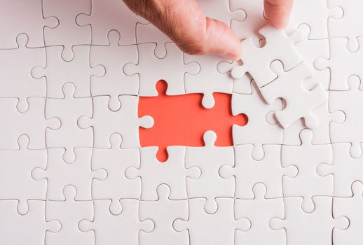 Top view flat lay of hand-holding last piece white paper jigsaw puzzle game last pieces put to place for solve problem complete mission, studio shot on a pink background, quiz calculation concept