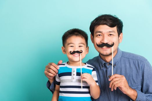 Family funny happy hipster father and his son kid holding black mustache props for the photo booth close face, studio shot isolated on a blue background, November men health awareness