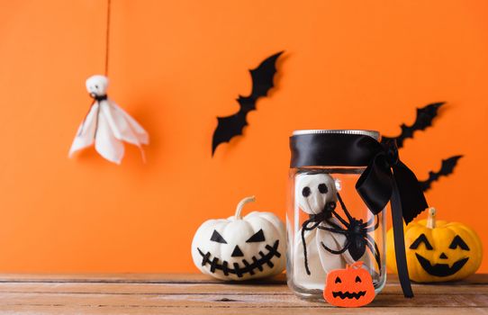 Funny Halloween day decoration party, Baby white ghost crafts scary face in jar glass and cute pumpkin ghost on wood table, studio shot isolated on orange background have spider and bats