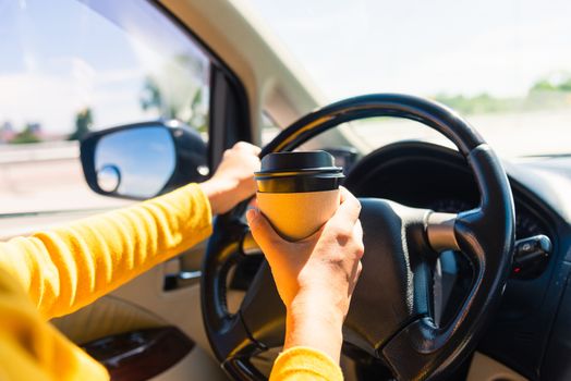 Asian woman drinking hot coffee takeaway cup inside a car and while driving the car in the morning during going to work on highway, Transportation and vehicle concept