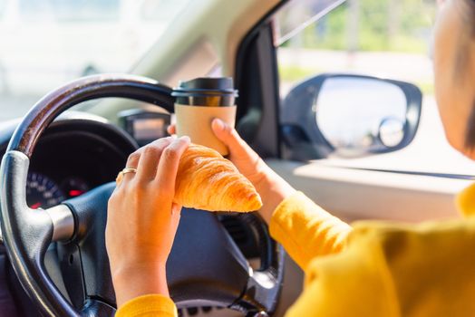 Asian woman eating food fastfood and drink coffee while driving the car in the morning during going to work on highway road, Transportation and vehicle concept