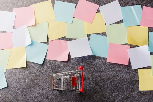 Above many blank paper stick note list with the shopping cart on concrete board, Shopping reminder memory today concept