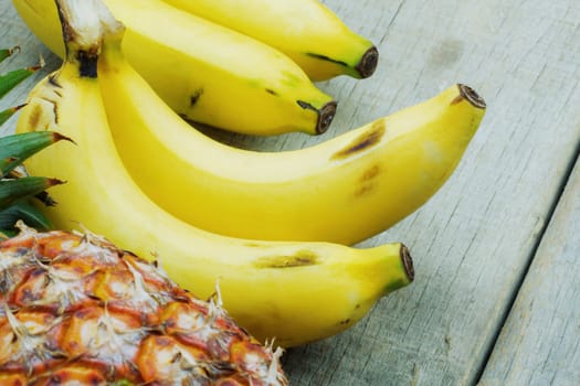 Ripe bananas and pineapple on wooden floor.