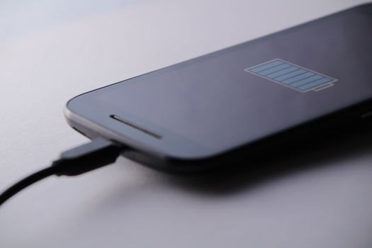 Smartphone charging battery with micro usb cable. White background.