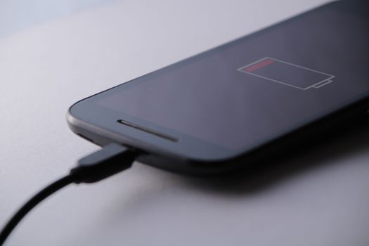 Smartphone charging battery with micro usb cable. White background.