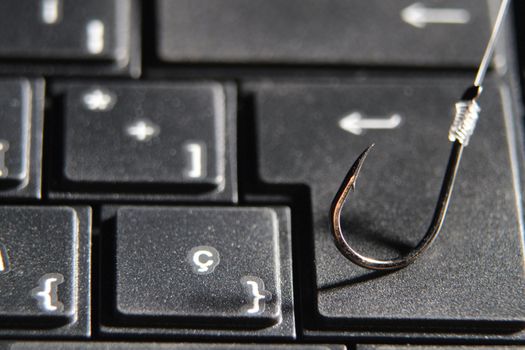 Conceptual picture of a hook on laptop keyboard suggesting cyber fraud and phishing