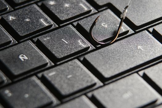 Conceptual picture of a hook on laptop keyboard suggesting cyber fraud and phishing