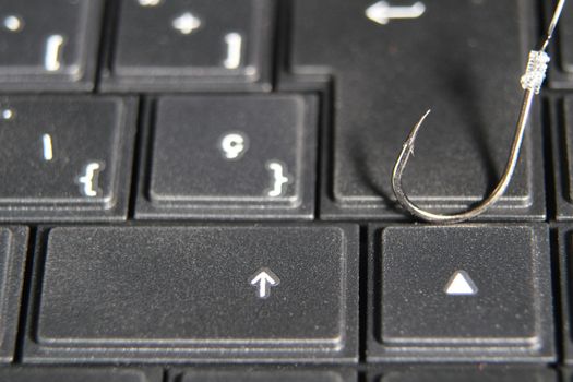 Conceptual picture of a hook on laptop keyboard suggesting cyber fraud and phishing