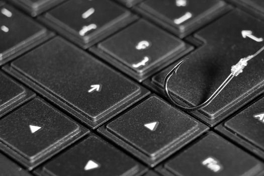 Conceptual picture of a hook on laptop keyboard suggesting cyber fraud and phishing