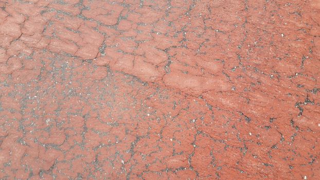 Red colored damaged road or paved pathway with crackes of different shpaes. Cracked texture with copy space for text and messages