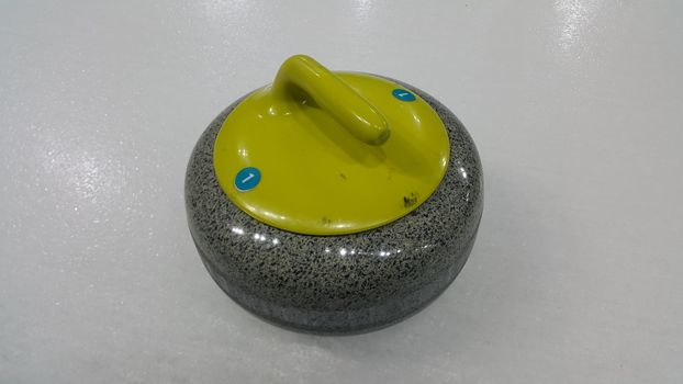 Top angular view of a curling stone on white slippery ice pitch in an arena for ice gmaes