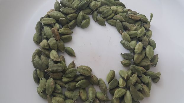 Closeup top view of dried green Elettaria cardamomum fruits with seeds, cardamom spice arranged in ring on a white background