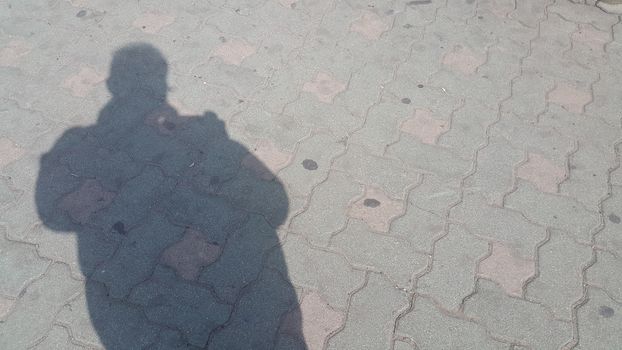 Silhouette: A Man's shadow on the red colored concrete ground under sunlight
