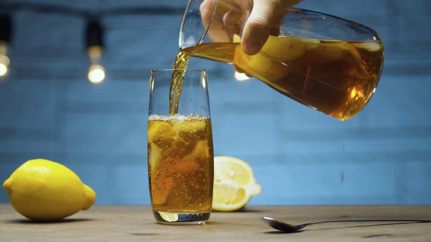 Close up male hand pouring ice tea into a glass. Blurry lamps on blue background