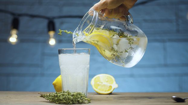 Close up pouring lemonade with thyme into a glass on blue background