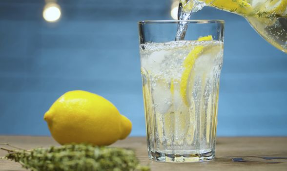 Close up pouring lemonade with thyme into a glass on blue background