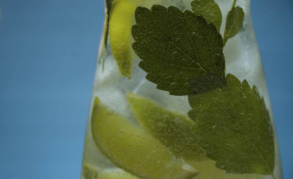 Close up lemonade with lime and mint in glass jug on blue background