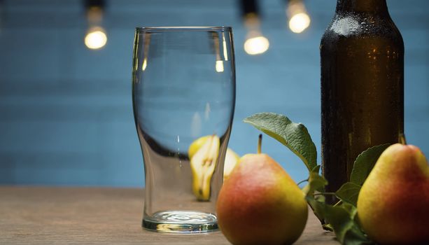 Close up male hand putting misted bottle of cider on the table on blue background. Fresh ripe pears. Healthy food, vitamins, fruits