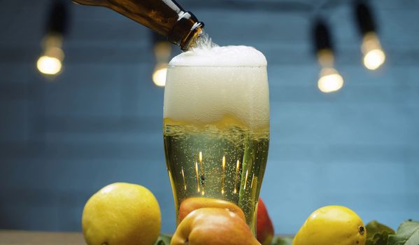 Close up delicious ripe pears and pear cider pouring into a glass on blue background. Healthy food, vitamins, fruits