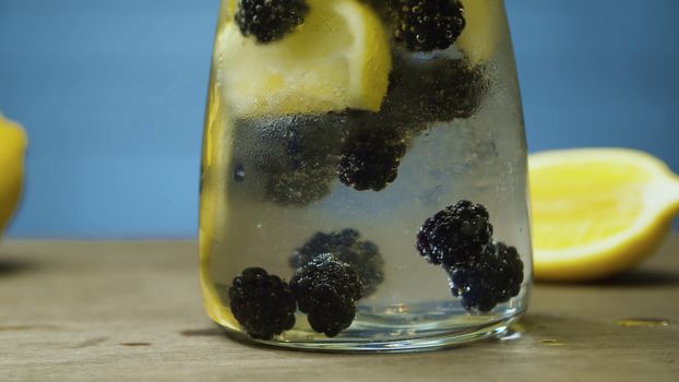 Close up dewberry lemonade in glass jug. Blurry lamps on blue background