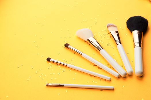 Makeup brushes in different sizes on a yellow background and glitter cropped look. High quality photo