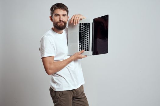 A man with a laptop in his hands on a light background in a white t-shirt emotions light background cropped view model portrait new technologies. High quality photo