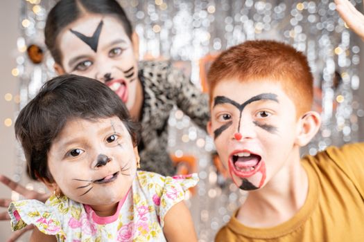 Group of kids in Halloween costumes gesticulating and making scary or spooky faces on decorated background by looking into camera