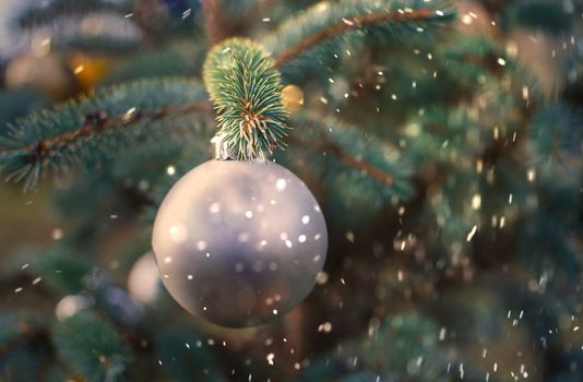 Christmas silver ball decoration ornament. Silver holiday ball hanging from a green christmas tree twig. New year greeting card.