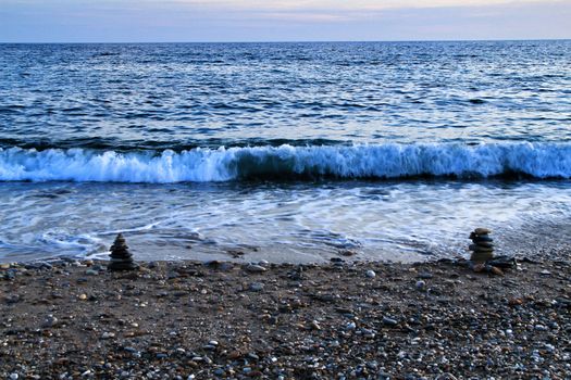 Round stacked stones on the Isla Plana beach at sunset in Cartagena. Waves in the background.