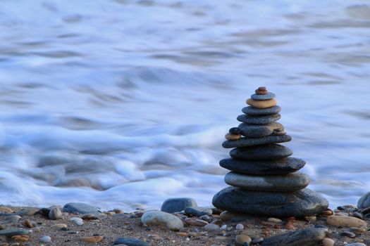 Round stacked stones on the Isla Plana beach at sunset in Cartagena. Waves in the background.