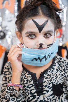 Vertical shot, Kid in Halloween witch dress and scary face removing medical mask by looking into camera.