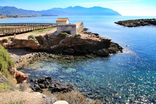 Old thermal baths on the beach with boulders, cliffs and mountains in Isla Plana village in Cartagena, Murcia, Spain in a sunny day