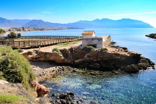 Old thermal baths on the beach with boulders, cliffs and mountains in Isla Plana village in Cartagena, Murcia, Spain in a sunny day