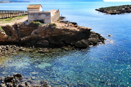 Old thermal baths on the beach with boulders, cliffs and mountains in Isla Plana village in Cartagena, Murcia, Spain in a sunny day