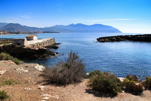 Beautiful beach with boulders, cliffs and mountains in Isla Plana village in Cartagena, Murcia, Spain in a sunny day