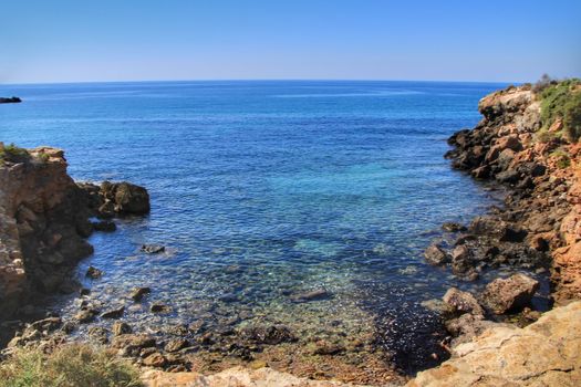 Beautiful beach with boulders, cliffs and mountains in Isla Plana village in Cartagena, Murcia, Spain in a sunny day