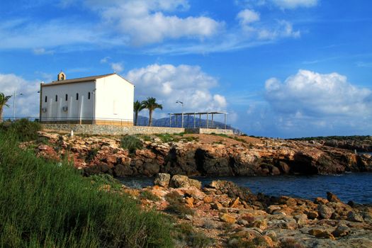 Old Virgen del Carmen hermitage built on the edge of a cliff in a cove in Isla Plana village, Cartagena, Spain