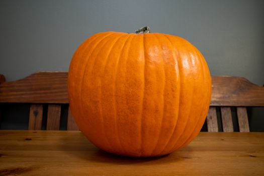 An orange pumpkin sits on a wooden kitchen table with two wood chairs behind it.