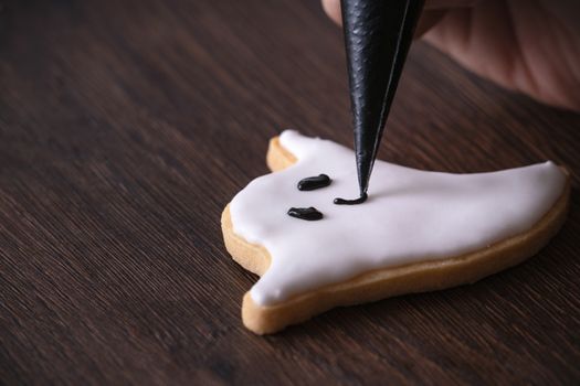 Close up of decorating cute Halloween ghost gingerbread cookies with frosting icing cream topping bag.