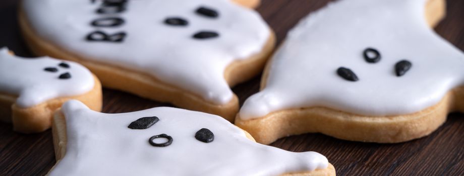 Close up of decorating cute Halloween ghost gingerbread cookies with frosting icing cream topping bag.