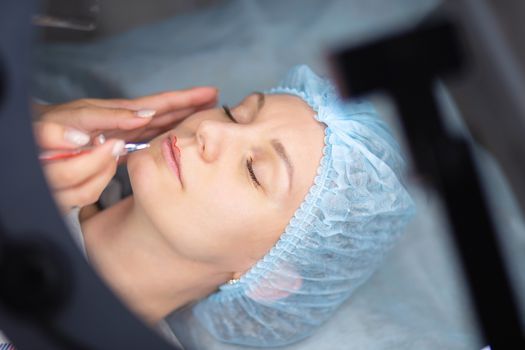 Preparation for permanent lip makeup. Drawing the contour of the lips for tattooing. Woman makes a tattoo on her face