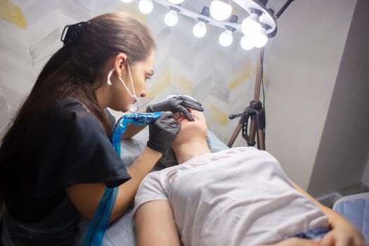 A woman makes permanent lip makeup to another woman in a beauty salon cabinet. Face tattoo. Modern trends in cosmetology